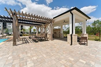 A patio with a pergola and a pool in the background.
